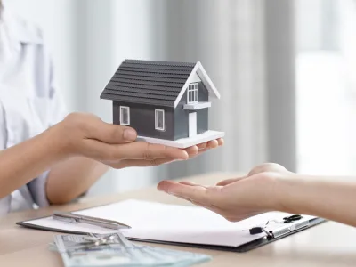 Close-up of a person handing over a miniature house, symbolizing asset division during divorce.