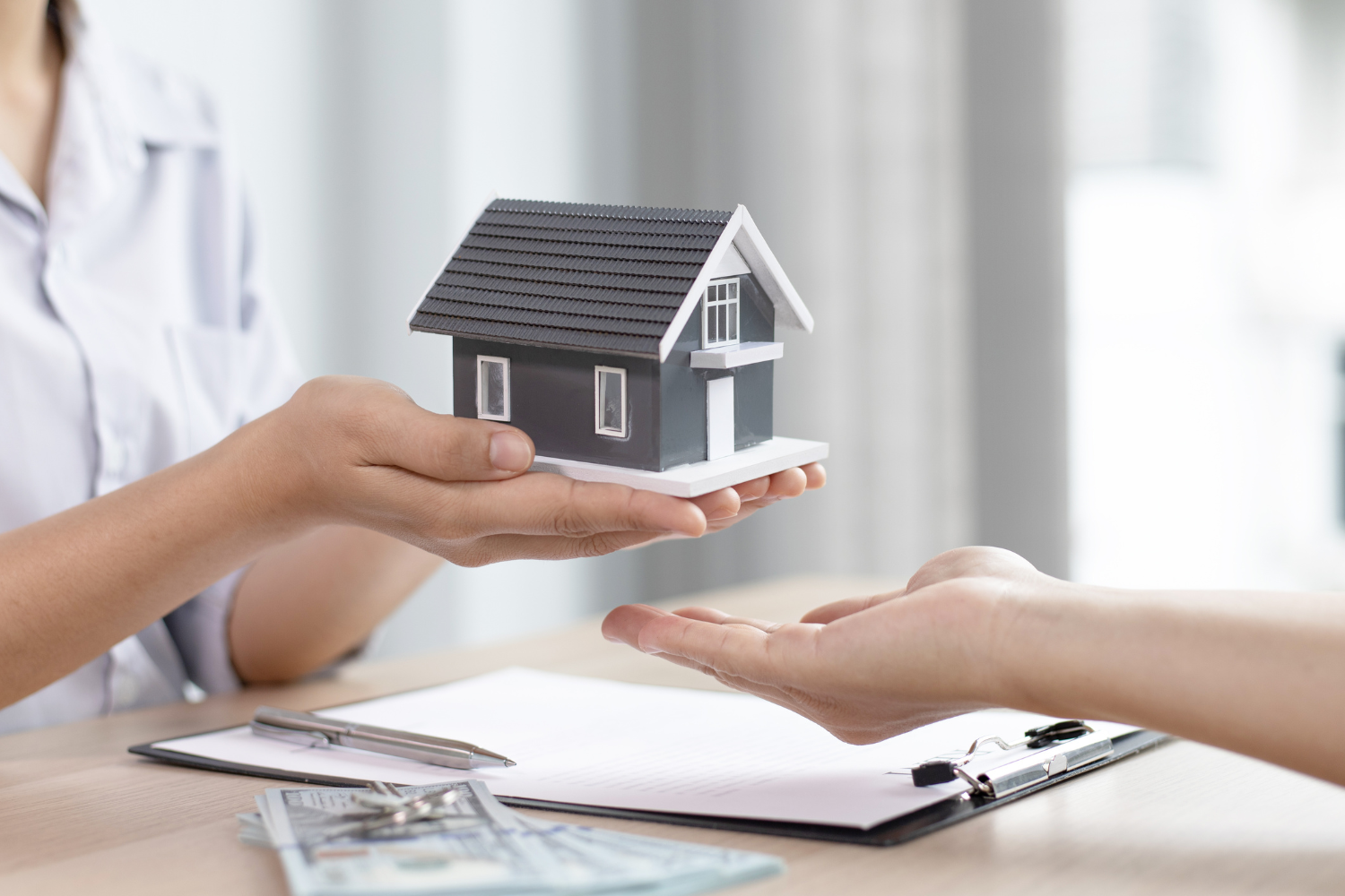 Close-up of a person handing over a miniature house, symbolizing asset division during divorce.